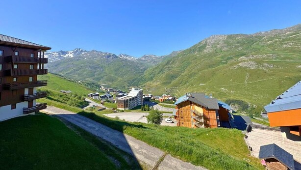 A mountain village with traditional wooden buildings, a paved road, and a clear view of snow-capped mountains in the background.