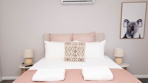 Een keurig opgeruimde hotelkamer met een bed, kussens, een wandairconditioner, een lijst met een afbeelding en nachtlampjes.