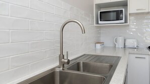 Een keuken met een witte betegelde spatwand, een roestvrijstalen spoelbak en witte kasten.