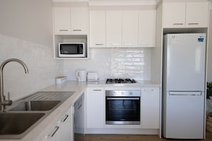 Une cuisine moderne avec des meubles blancs, un évier en acier inoxydable, un four à micro-ondes, un four traditionnel, une cuisinière à gaz et un réfrigérateur.