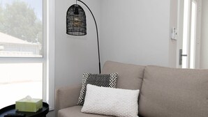 Een sofa in neutrale tinten met gestreepte kussens, een zwarte vloerlamp en een klein bijzettafeltje met een afstandsbediening en zakdoekjes.