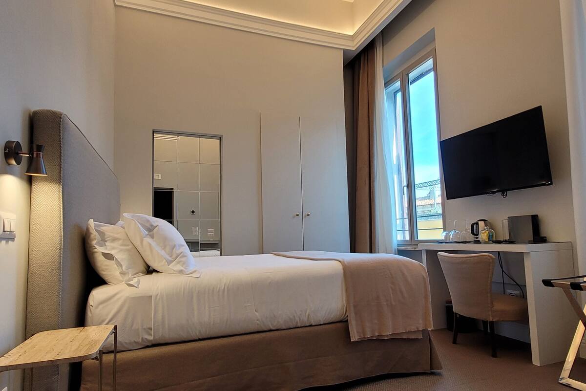 A hotel room with a bed, a desk, a chair, a TV, and a window with a view.
