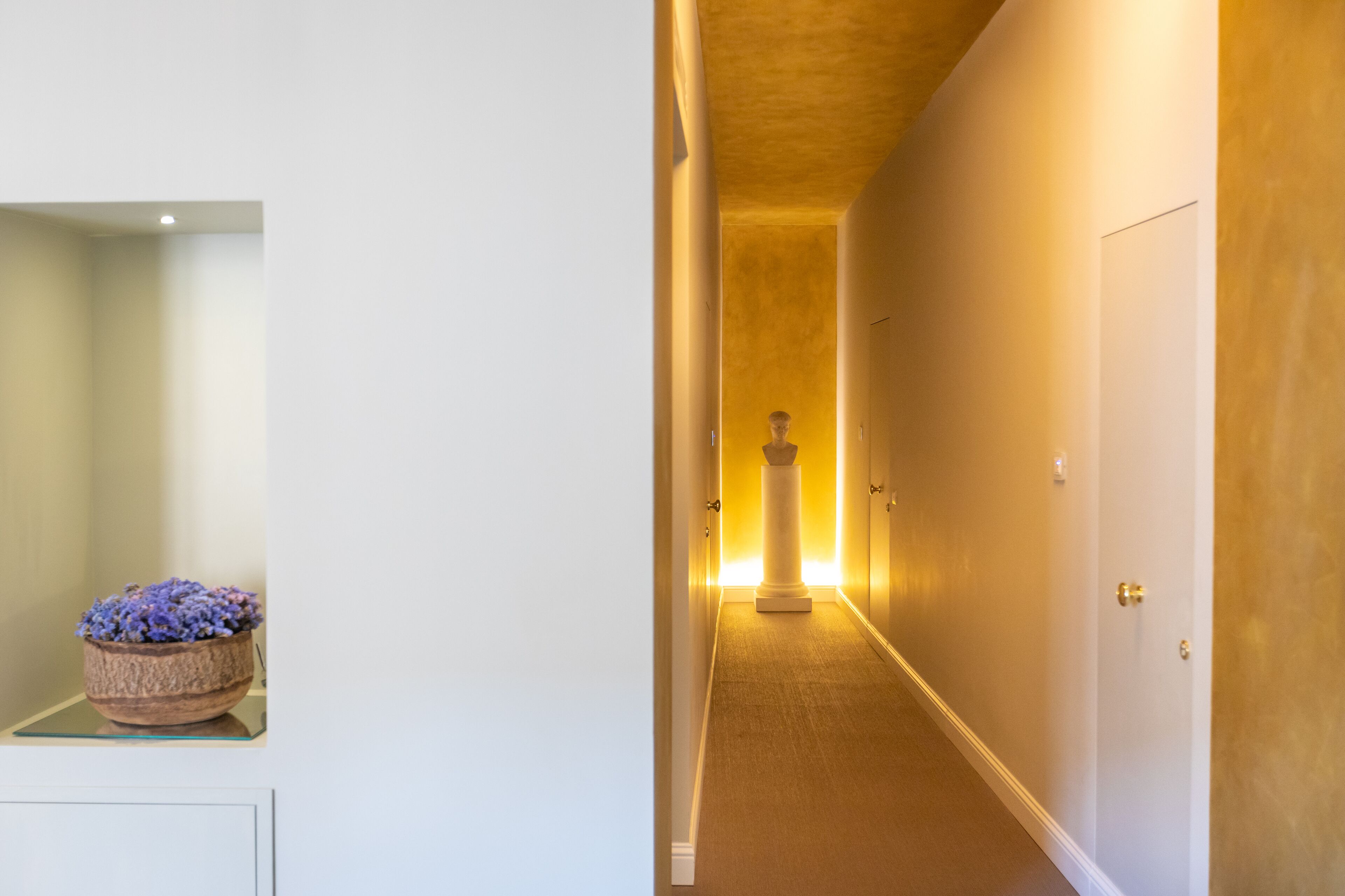Un couloir avec un pot de fleurs, un pilier et une porte.