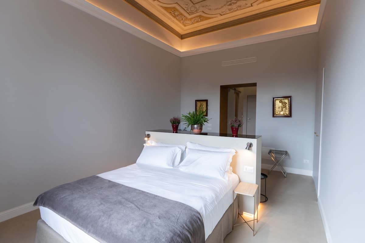 A modern bedroom with a large bed, bedside tables, a mirror, and decorative plants.