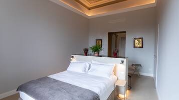 Un dormitorio moderno con una cama grande, mesitas de noche, un espejo y plantas decorativas.