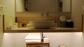Une salle de bain avec un grand lavabo sur colonne, un miroir, un porte-serviettes et une poubelle.