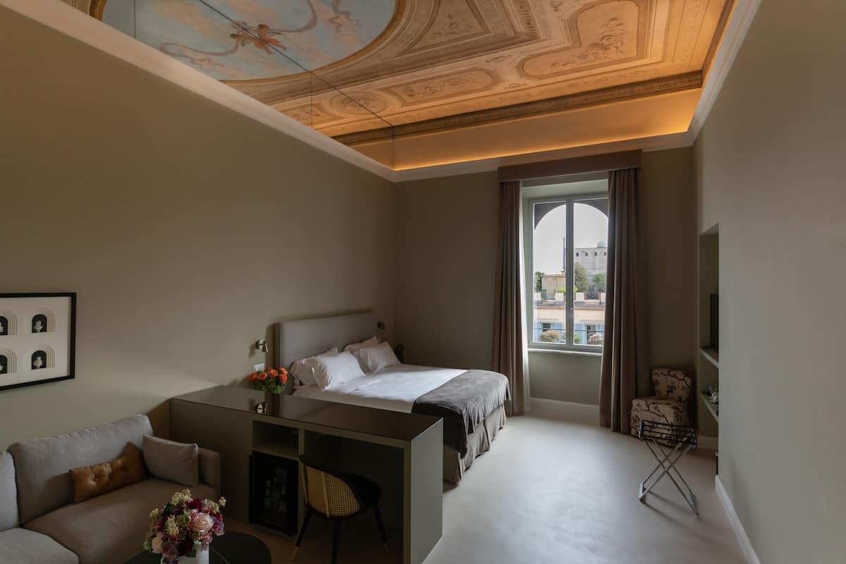 A hotel room with a bed, a desk, a chair, a TV, and a window with a view of a building.