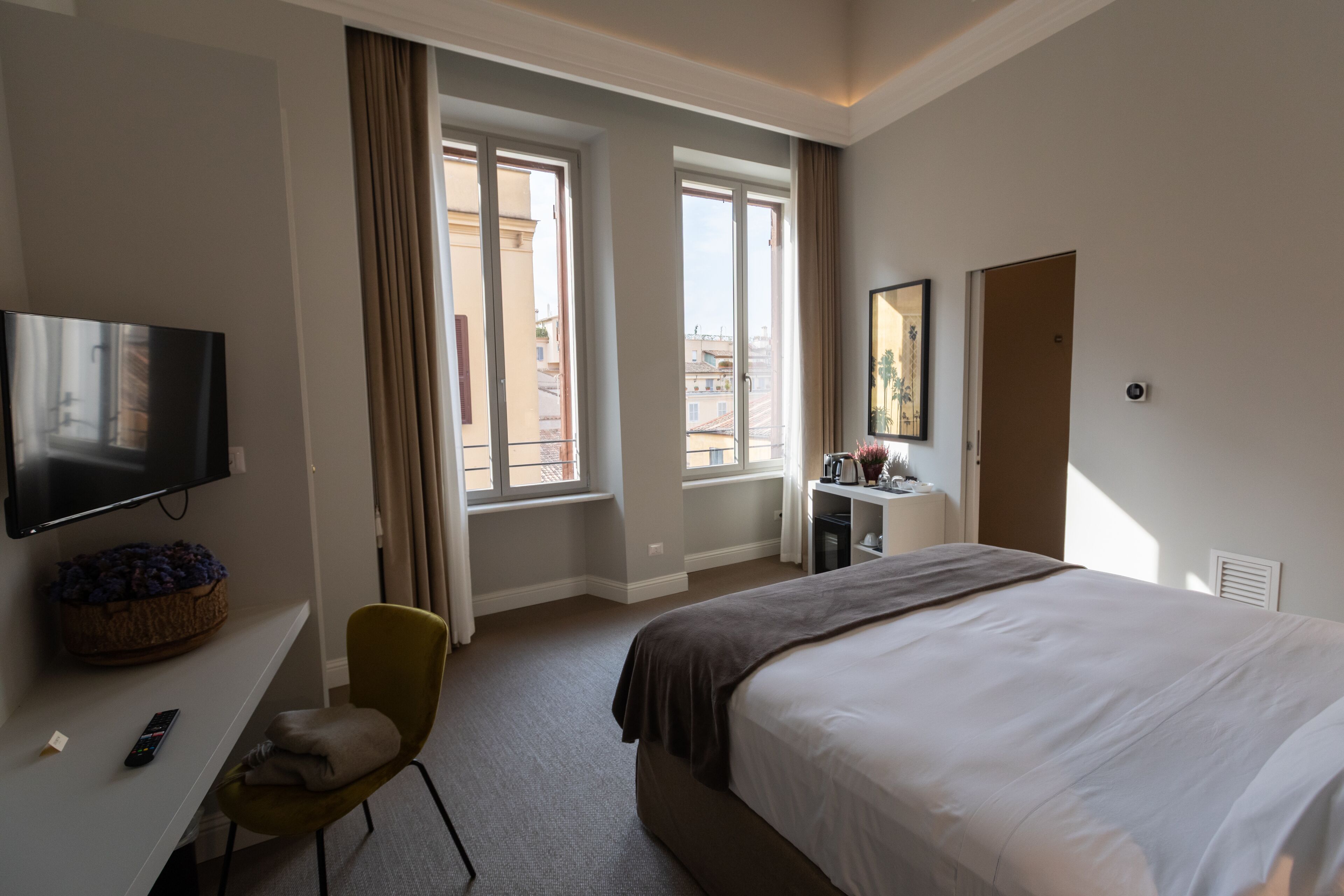 Una camera d'albergo con un letto, una TV, una scrivania, una sedia e una finestra con tende.