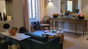 Ein modernes Wohnzimmer mit einem grünen Sofa, einem Esstisch mit Blumenvase, einem großen Spiegel und einer Chandeliebre.