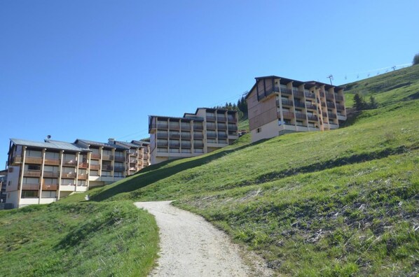 A hillside with a gravel path leading to a row of multi-story buildings with balconies.