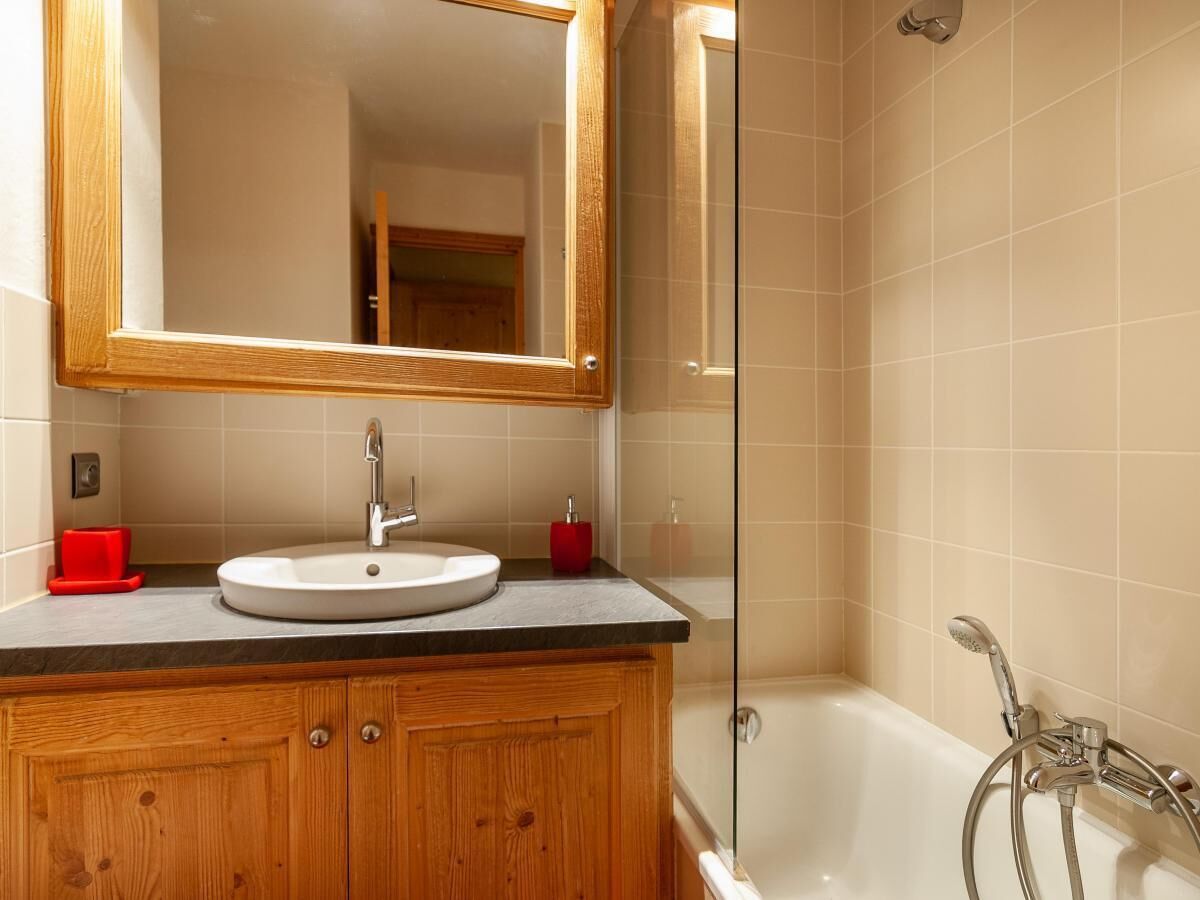 Une salle de bain avec un meuble-lavabo en bois, un lavabo rond, un miroir et une cabine de douche en verre.