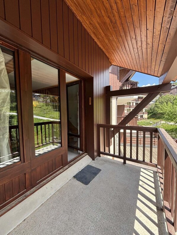 A wooden balcony with a glass door leading to an interior space, a wooden railing, and a doormat on the floor.