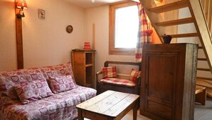Ein gemütliches Zimmer mit einer Holztreppe, einem Sofa, einem kleinen Tisch und einem Fenster mit Vorhängen.