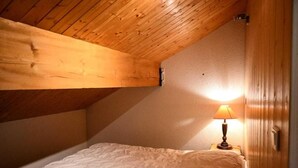Ein Einzelbett in einem Zimmer mit Holzbalkendecke, einer Nachttischlampe und einem Holzschrank.