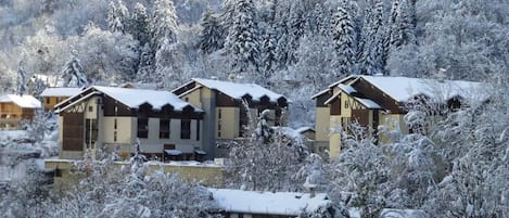 A snow-covered resort with multiple buildings, including a lodge and guest houses, surrounded by trees.