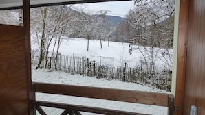 Ventana con marco de madera que ofrece vistas a un paisaje nevado, con árboles y una cerca.