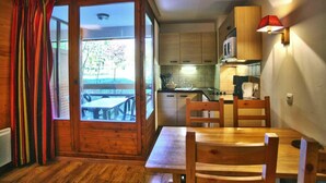 Acogedora habitación estilo cabaña con una mesa de comedor y sillas, armarios de madera, una zona de cocina y un gran ventanal corredero que da a un área exterior con asientos.