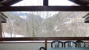 A covered outdoor area with a table and chairs, a view of trees and mountains through the roof, and a wooden beam structure. - 5th floor, balcony, tv, 56m², Brides Les Bains (Brides-les-Bains)