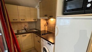 A compact kitchen with a washing machine, a microwave, and wooden cabinets. - 5th floor, balcony, tv, 56m², Brides Les Bains (Brides-les-Bains)