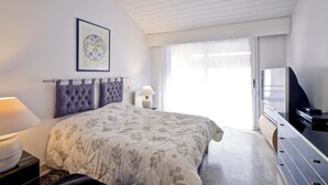 A modern bedroom with a large bed, a television, and a window with sheer curtains.