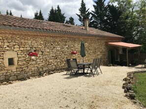 A stone building with a tiled roof, a small window, and a patio area with a table and chairs.
