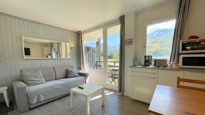 Un salon moderne comprenant un canapé, une table basse et une table à manger. Il y a également un coin cuisine avec un four à micro-ondes et une fenêtre donnant sur un paysage pittoresque.