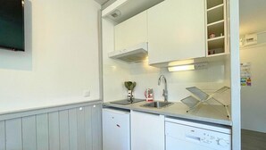 Une cuisine compacte avec des meubles blancs, un lave-vaisselle encastré, un four à micro-ondes et un évier avec un robinet.