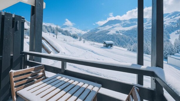 Un paysage de montagne enneigé, avec une cabane et des traces de ski visibles depuis un balcon.