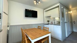 Une cuisine compacte avec une table et des chaises en bois, un four encastré et un téléviseur fixé au mur.