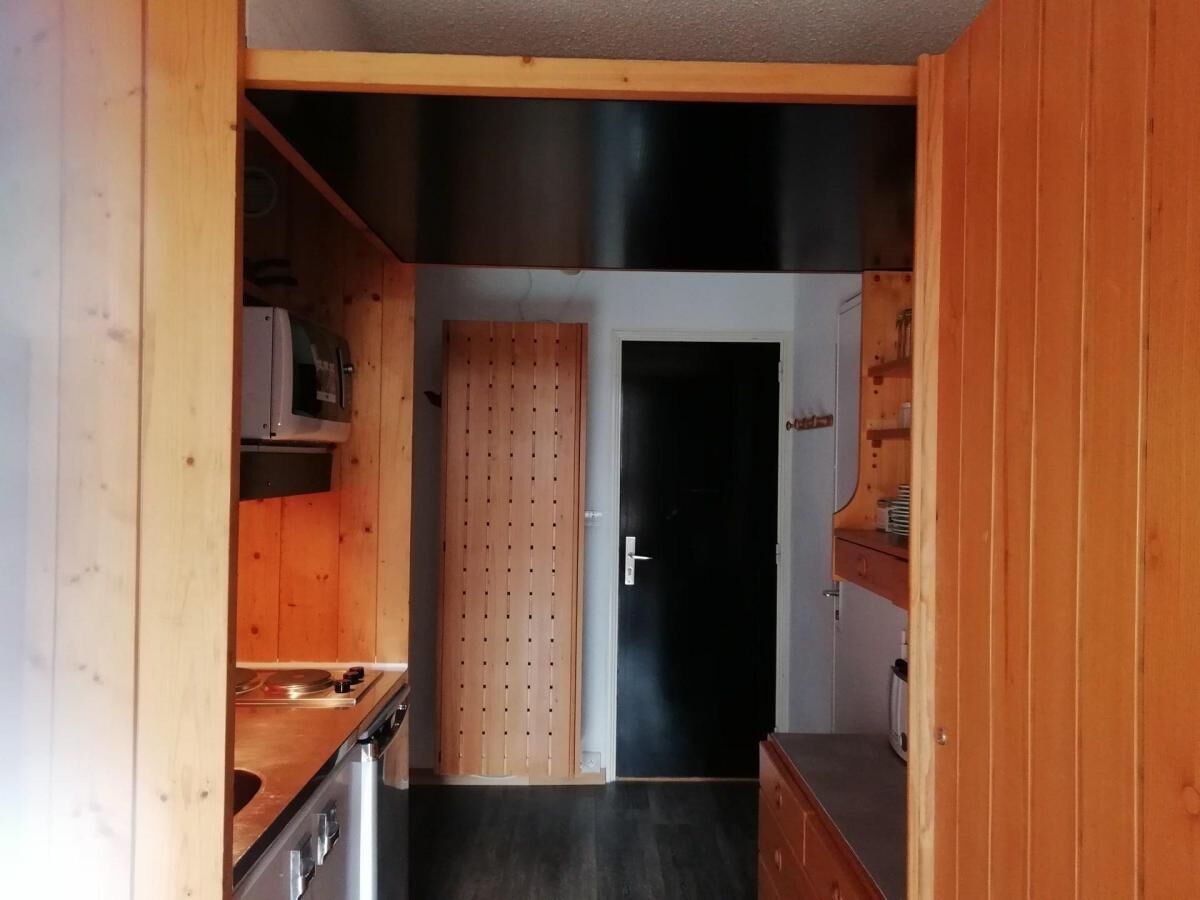 A narrow kitchen with wooden cabinets, a microwave, and a door leading to another room.