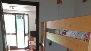 Ett rum med en våningssäng, ett trägolv, ett matbord med stolar och en utsikt genom en öppen dörr ut mot en balkong.