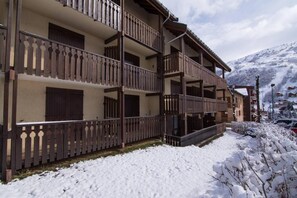Ein mehrstöckiges Hotel mit Balkonen, verschneiter Umgebung und einem Bergpanorama im Hintergrund.