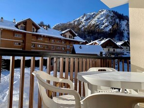 En træterrasse med et bord og stole, med udsigt over et sneklædt bjerg og bygninger.