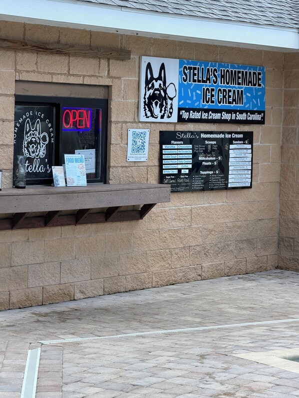 Un escaparate con un letrero de neón que dice 'ABIERTO', un panel con el menú y un anuncio que promociona 'Stella's Homemade Ice Cream' como la heladería mejor calificada en Carolina del Sur.