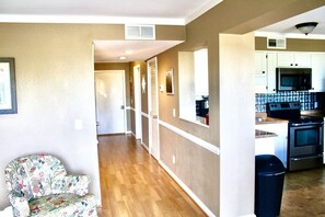 A hallway leading to a kitchen with wooden flooring, white cabinets, and a microwave.
