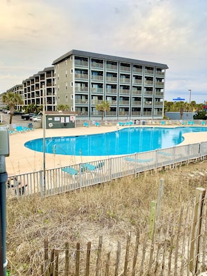 A hotel with a large swimming pool, multiple balconies, and a parking area.