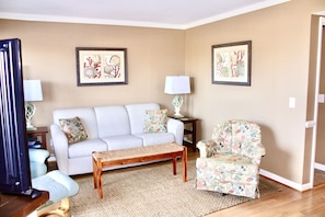 A living room with a sofa, a chair, a bench, two lamps, and two framed pictures on the wall.