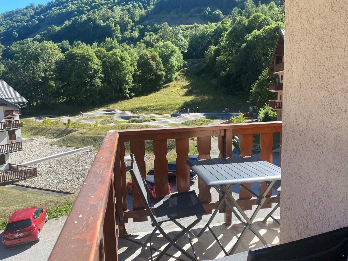 A balcony with a table and chairs, overlooking a parking area and a mountainous landscape.