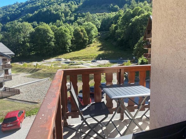 A balcony with a table and chairs, overlooking a parking area and a mountainous landscape.