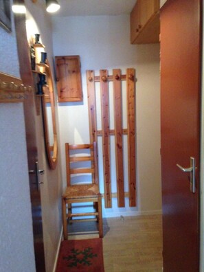 Un pasillo estrecho con una silla de madera, un revestimiento de listones de madera y una puerta roja.
