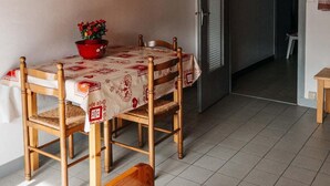 Ein Essbereich mit Holztisch und -stühlen, einem roten Blumentopf und einer Tischdecke mit Muster.