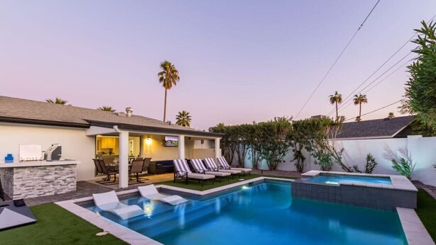 Un jardin avec une piscine, des chaises longues, un espace barbecue et des palmiers.