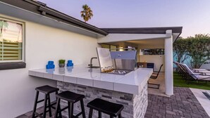 Une cuisine extérieure dotée d’un bar, comprenant des tabourets, un barbecue et un espace détente avec des fauteuils confortables.