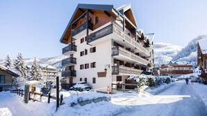 A multi-story building with balconies, a snow-covered street, and mountains in the background. - 50m from ski slopes, 3rd floor, balcony, tv, ski locker, 27m², Valloire (Valloire)