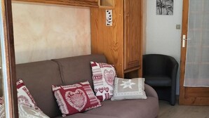 A living room with a sofa, pillows, a wooden cabinet, a chair, and a door. - 50m from ski slopes, 3rd floor, balcony, tv, ski locker, 27m², Valloire (Valloire)