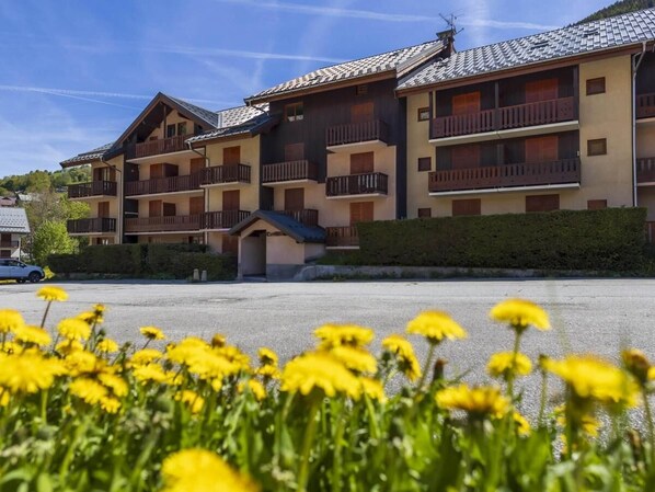 A multi-story hotel with balconies, a parking area, and yellow flowers in the foreground.