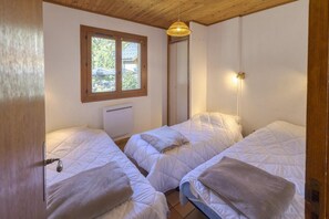 Une chambre avec deux lits, une fenêtre, un radiateur et un luminaire suspendu.