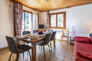 Un coin repas avec une table en bois, des chaises et un téléviseur en arrière-plan.