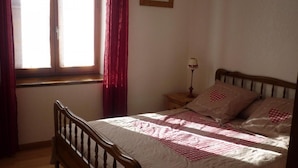 A bedroom with a wooden bed, a nightstand with a lamp, and a window with curtains.