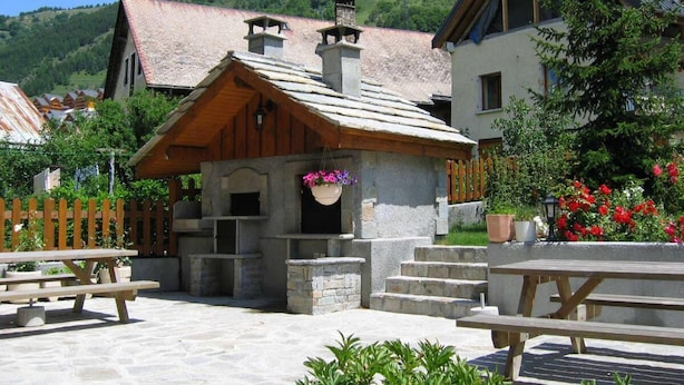 A rustic mountain lodge with stone walls, wooden beams, and a stone staircase leading to a wooden porch.